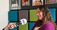 Frau sitzt in einem Raum mit Gold-Auszeichnungen an der Wand und wird per Mikrofon interviewt